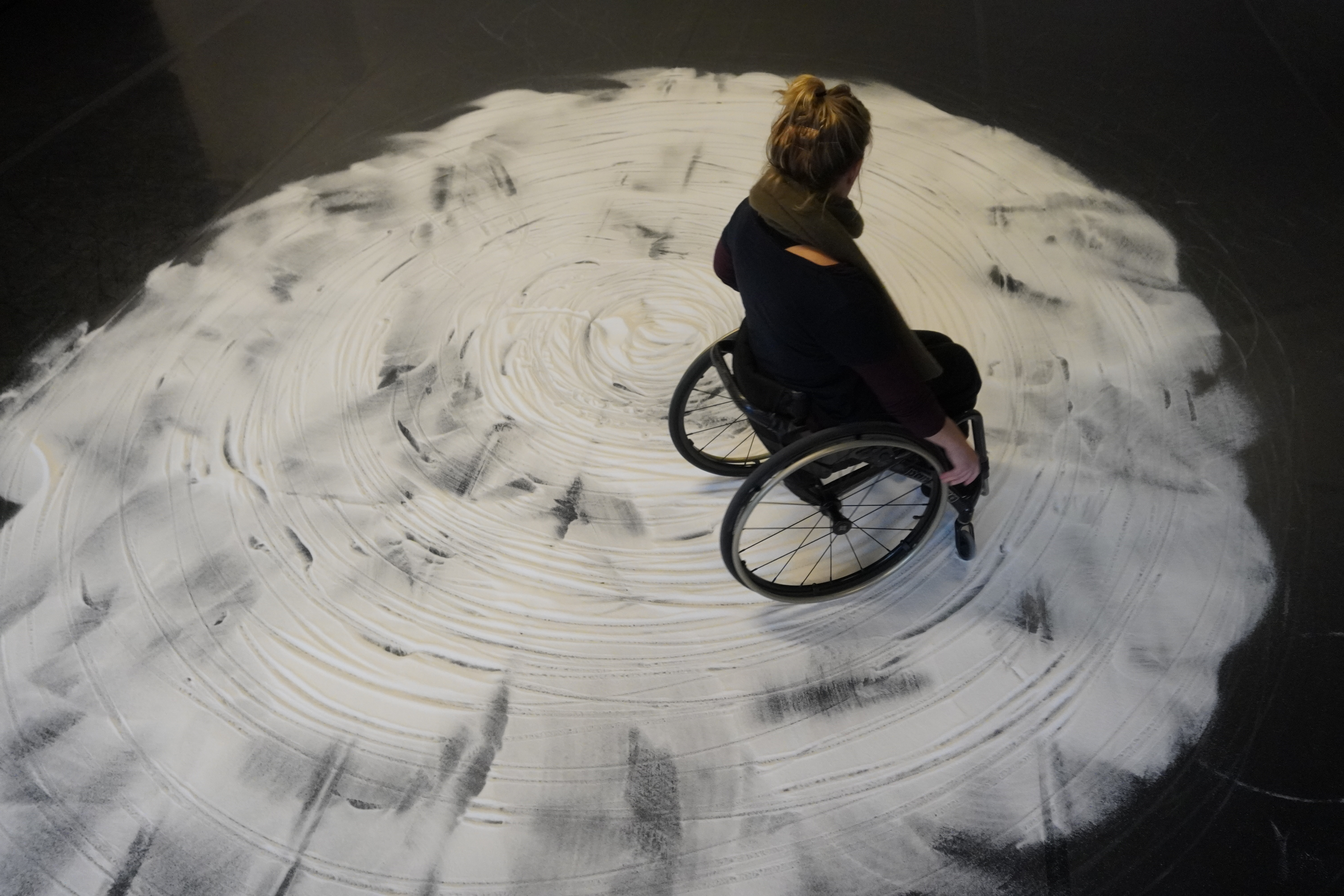 A crip dancer, Madeleine, is seen from above on a white salty floor rolling on her wheels