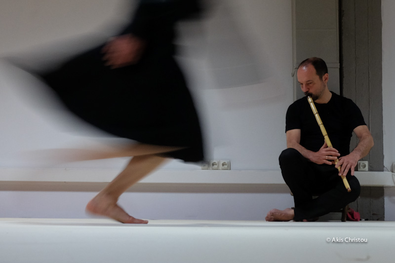 A musician and a female performer dressed in black in a white attic 