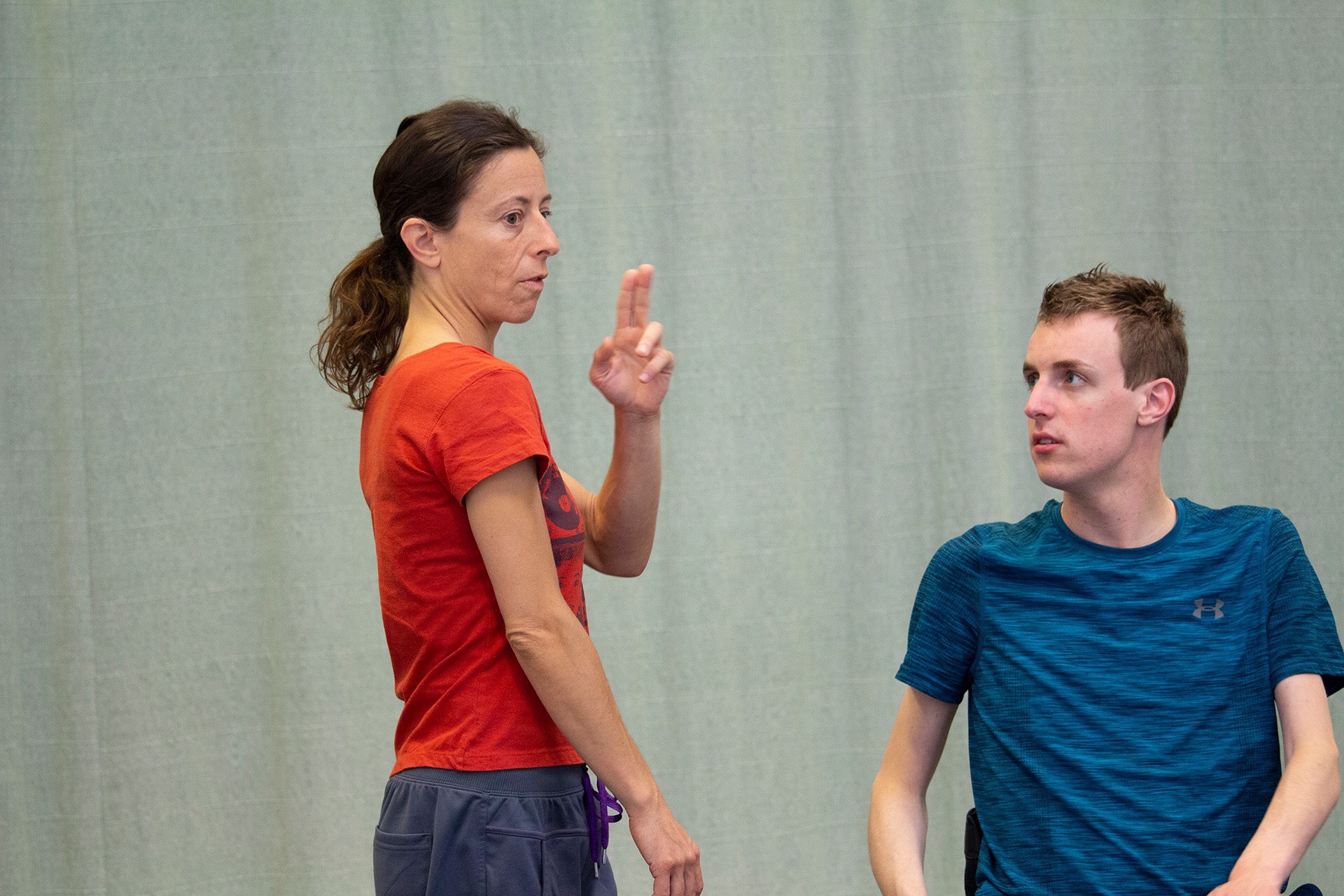 A crip dancer, Sander, wearing a blue t-shirt looks carefully at Maria wearing an orange t-shirt and grey pants wearing 