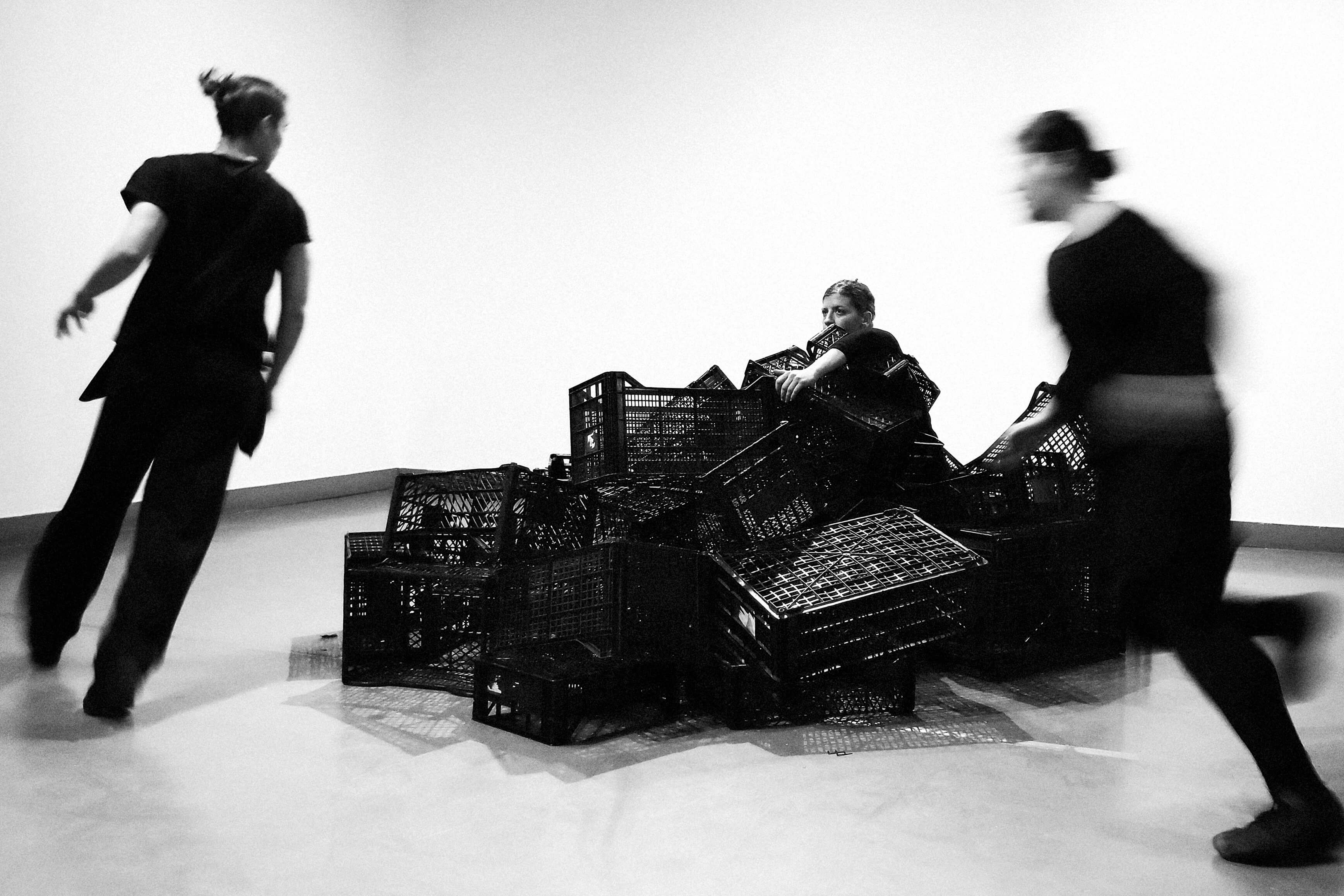 Three dancers move around a pile of crates