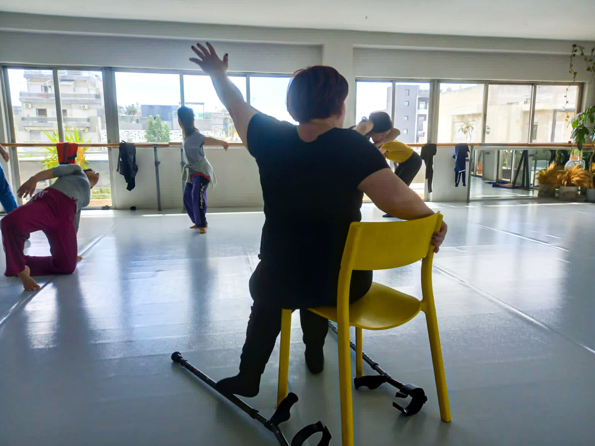 a crip dancer dressed in black sits on yellow chair raising her left arm high