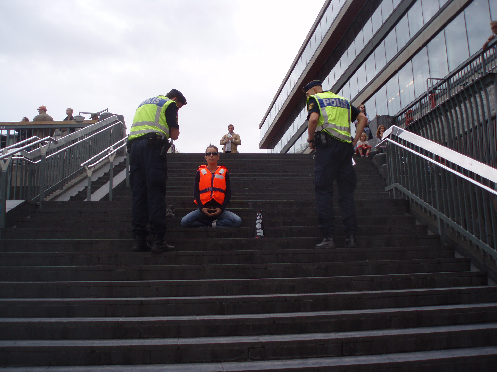 two officers stand on each side of a performer who sits on a staircase wearing a life vest 