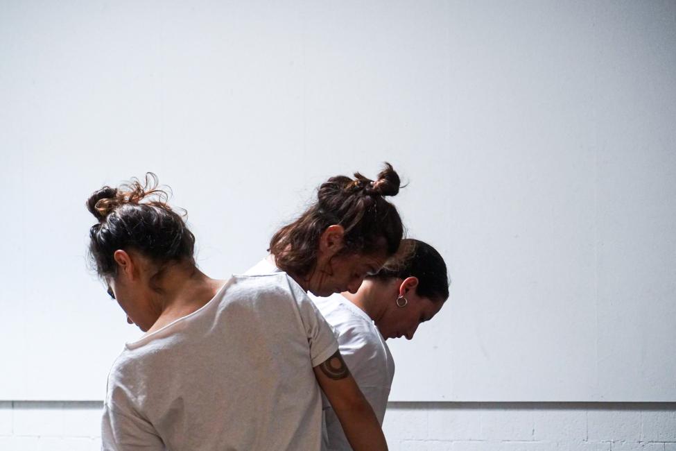 Dancing (fancy), three female performers wearing white t-shirts appear in a line one behind the other with their torso and head leaning slightly.