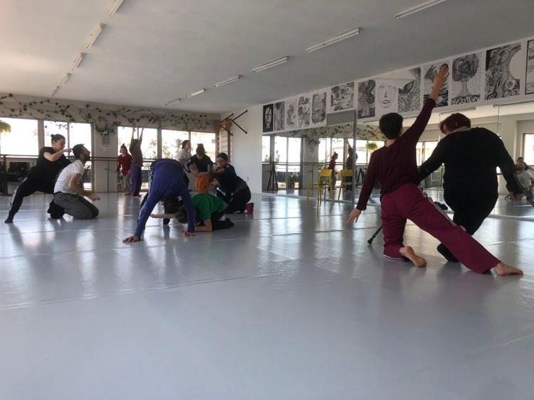 a group of performers moving in a white dance studio space