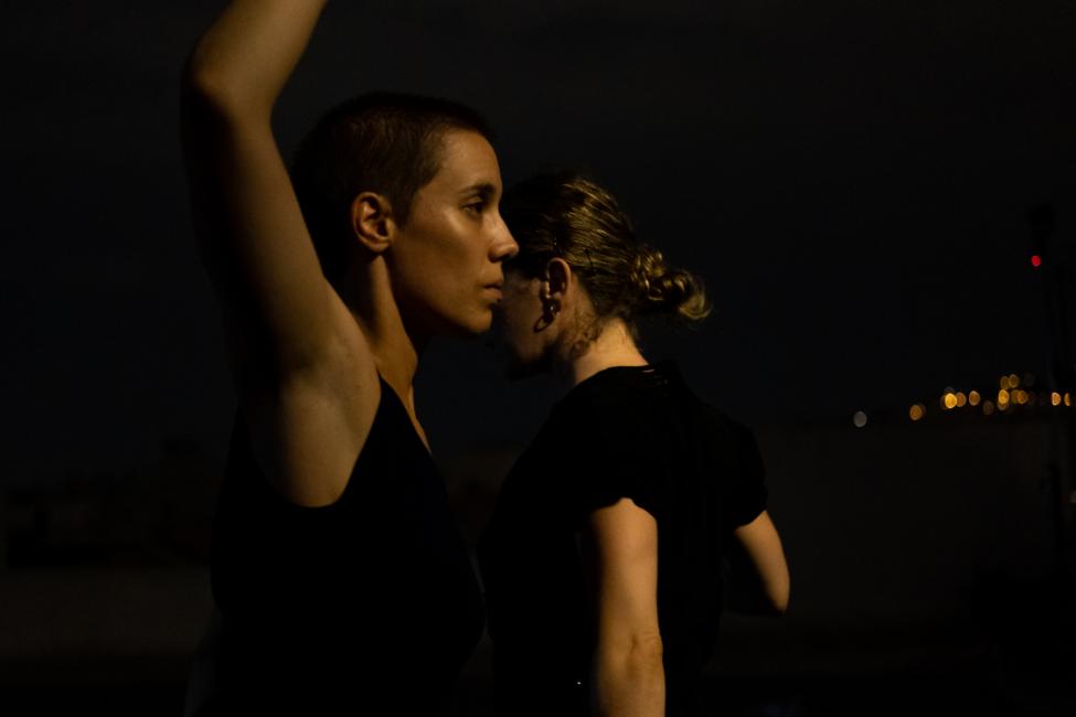 two women, the one infront is seen with her arm raised sideways in a gesture of revolution