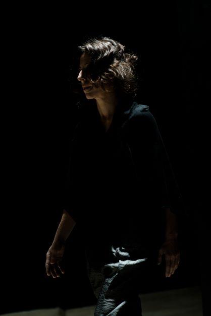 Maria, a performer dressed in black, faces front