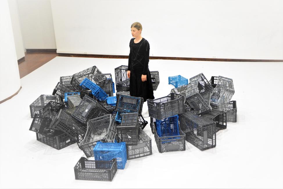a female dancer stands in a terrain of solitude with crates scattered around her