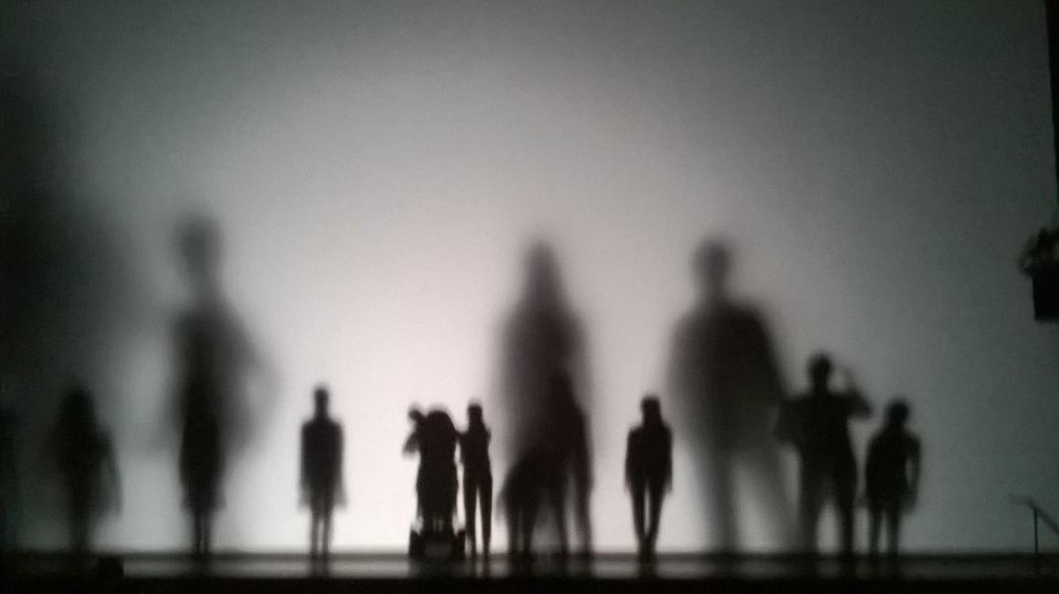 Performers of different heights walk behind a screen