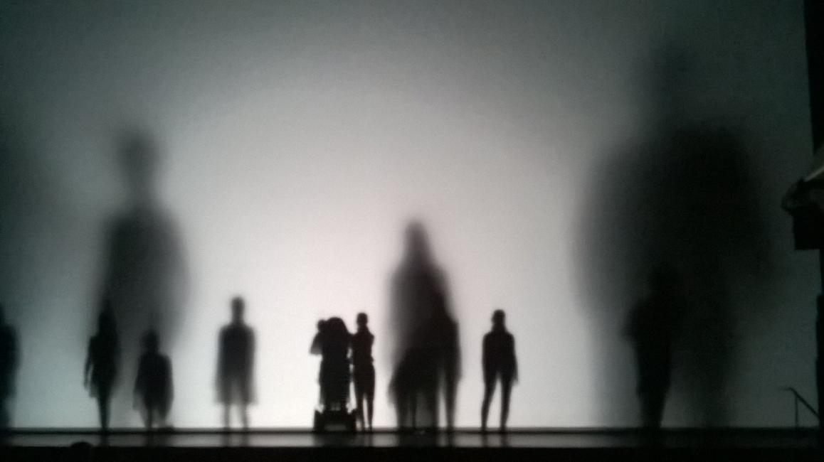 Performers of different heights walk behind a screen